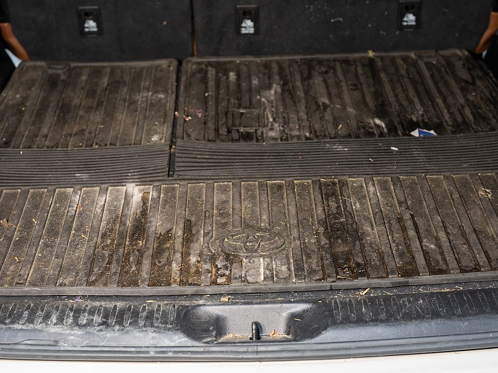 Cargo area of a white Toyota Highlander before detailing, with dried mud, leaves, and grass across the rubber cargo mat