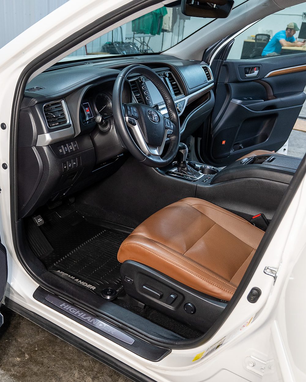 The same Toyota Highlander front interior after detailing, with a clean floor mat, dressed dashboard and console, and a clean lit door sill
