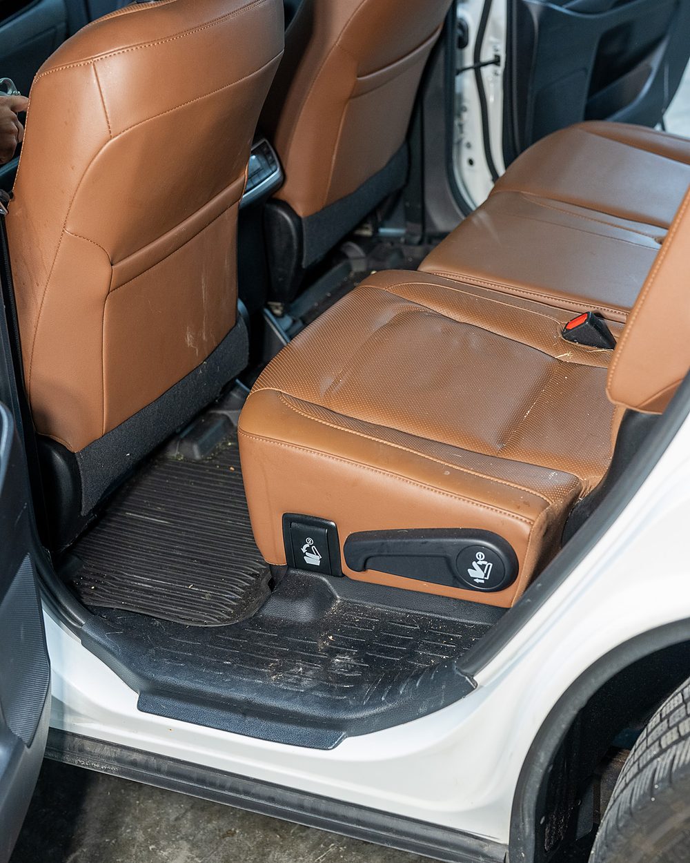 Second-row seat and floor of a white Toyota Highlander before detailing, with soil worked into the tan leather seams and debris through the rear floor mat