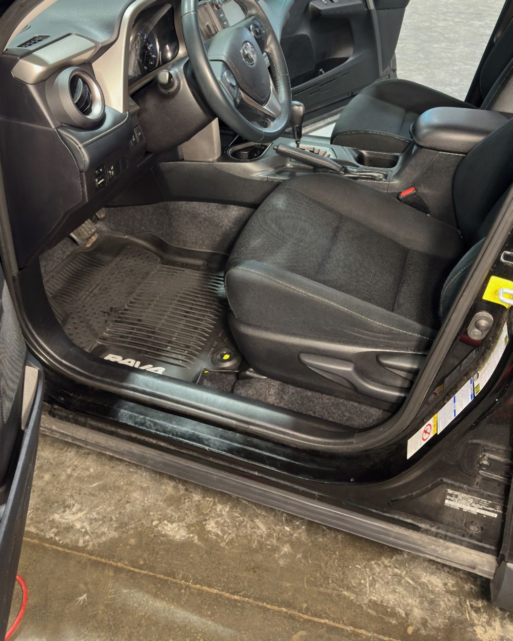 The same Toyota RAV4 footwell after detailing, with the floor mat, door sill, and rocker panel cleaned and the carpet dark again
