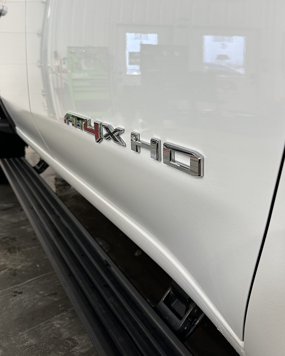 The same pickup door and rocker after an exterior detail, with clean white paint reflecting the shop lights and a bright chrome badge